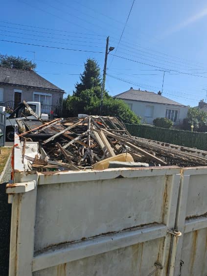 Benne remplie de charpente, tuiles et gravats après la dépose d'une toiture sur une maison