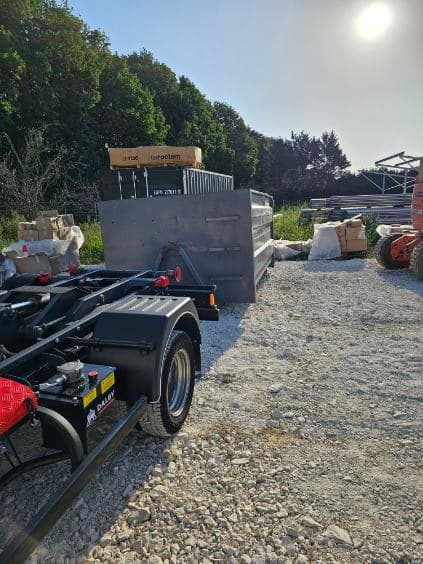 Benne vide posée sur un terrain en chantier à côté du camion porte-benne PETRY