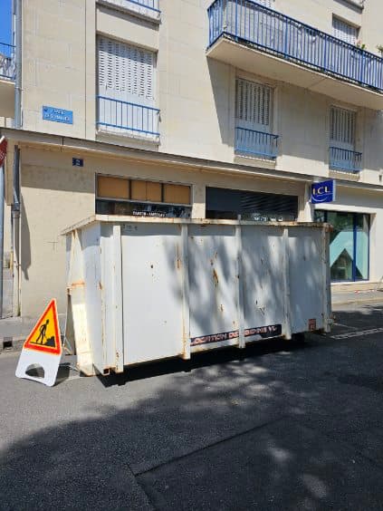 Benne de location VL déposée le long d'un trottoir avec panneau de signalisation de travaux